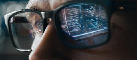 Person wearing glasses with reflection of monitor seen in glass lens